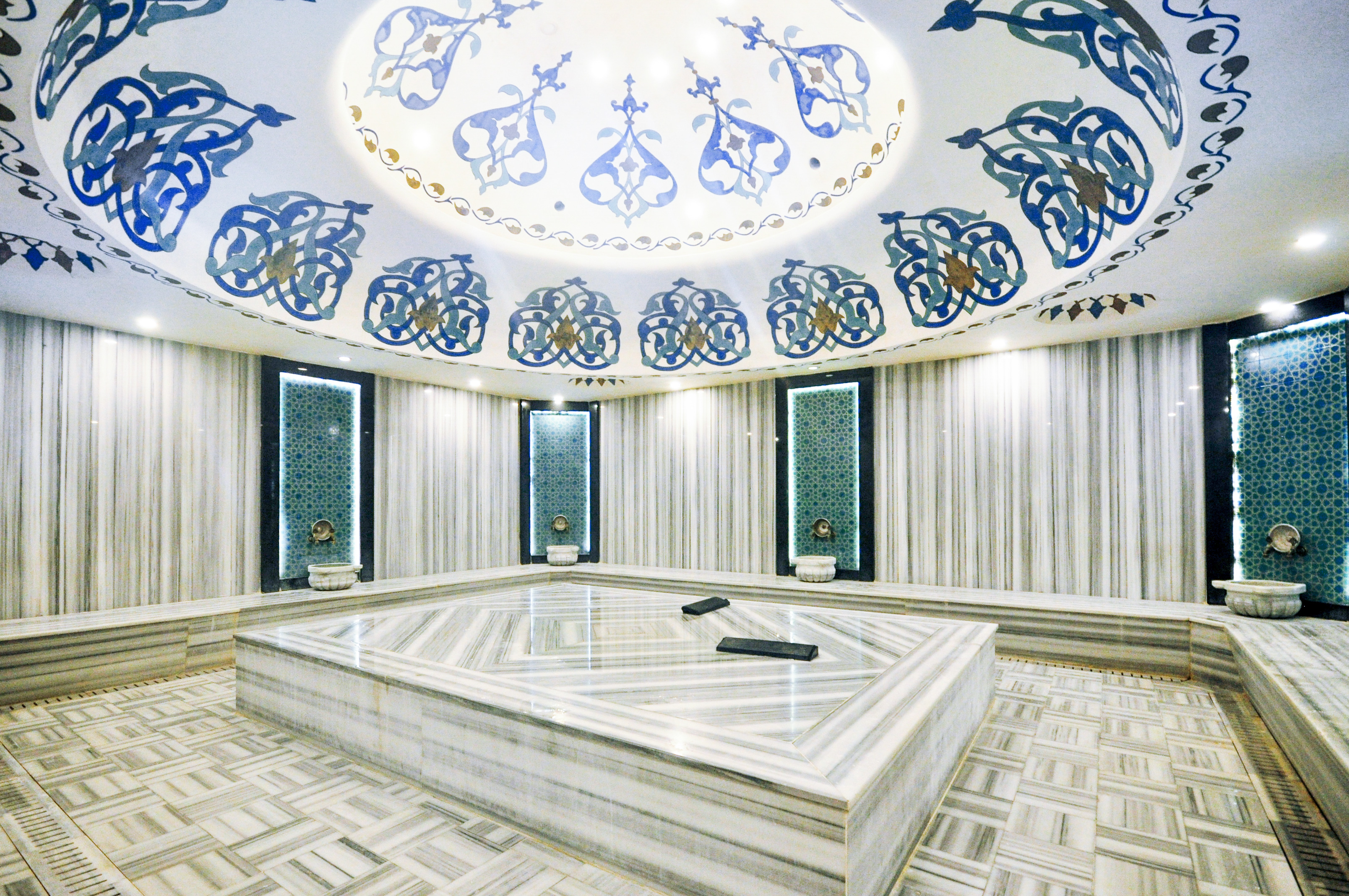Hammam with a marble platform and bowls beneath a patterned domed ceiling in a complex with apartments