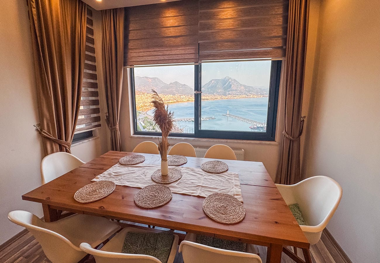 Dining room with a wooden table and six white chairs beside sea and mountain views in Türkiye for sale