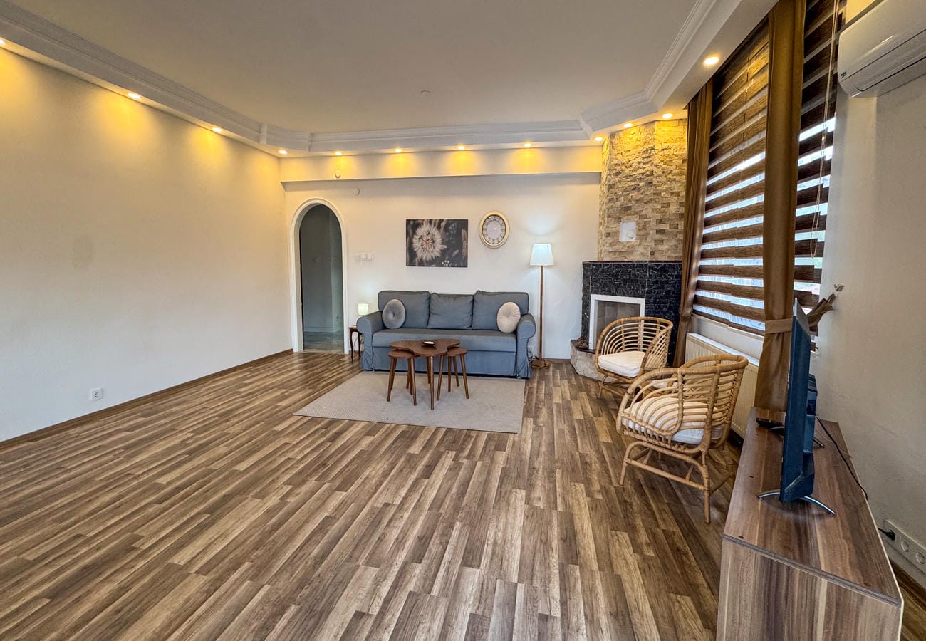 Living room with a grey sofa, stone-clad fireplace and wicker armchairs in a flat for sale