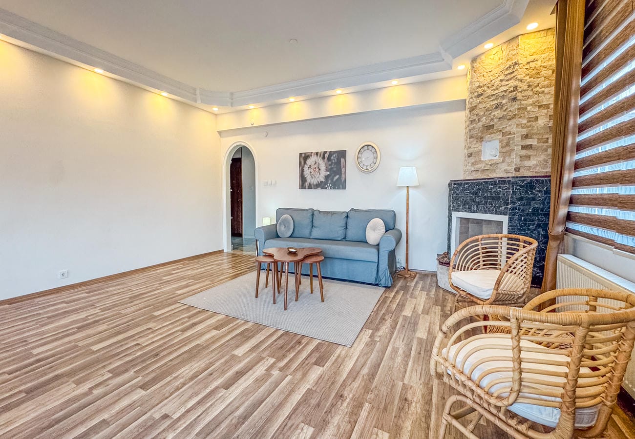 Living room with a grey sofa, wicker armchairs and stone-clad fireplace in an apartment in Alanya