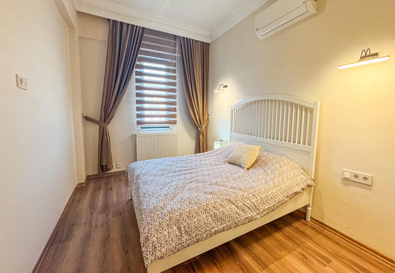 Bedroom with a double bed, striped roller blind and brown curtains in a flat