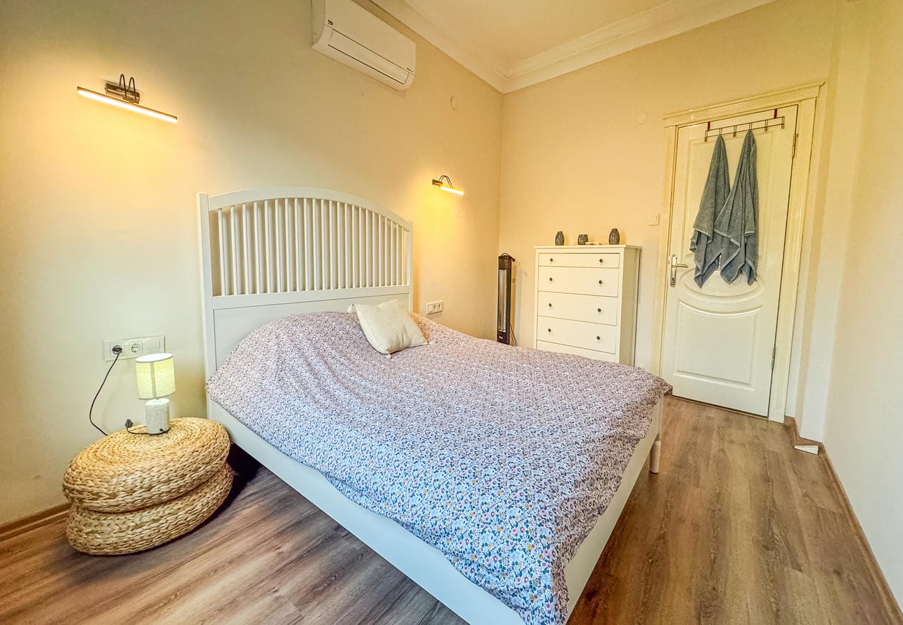 Bedroom with a double bed, white chest and wicker bedside tables in an apartment