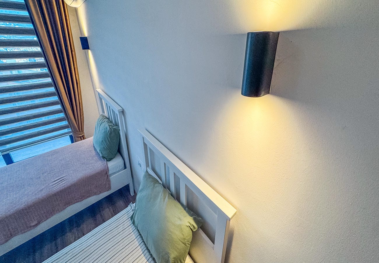 Bedroom with two single beds, green cushions and a panoramic window in a flat