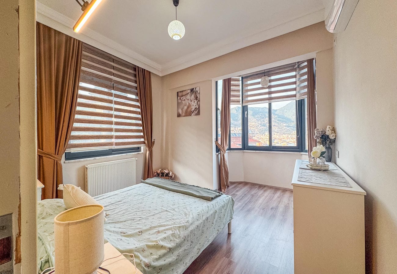 Bedroom with a double bed and panoramic corner window overlooking mountains in Alanya