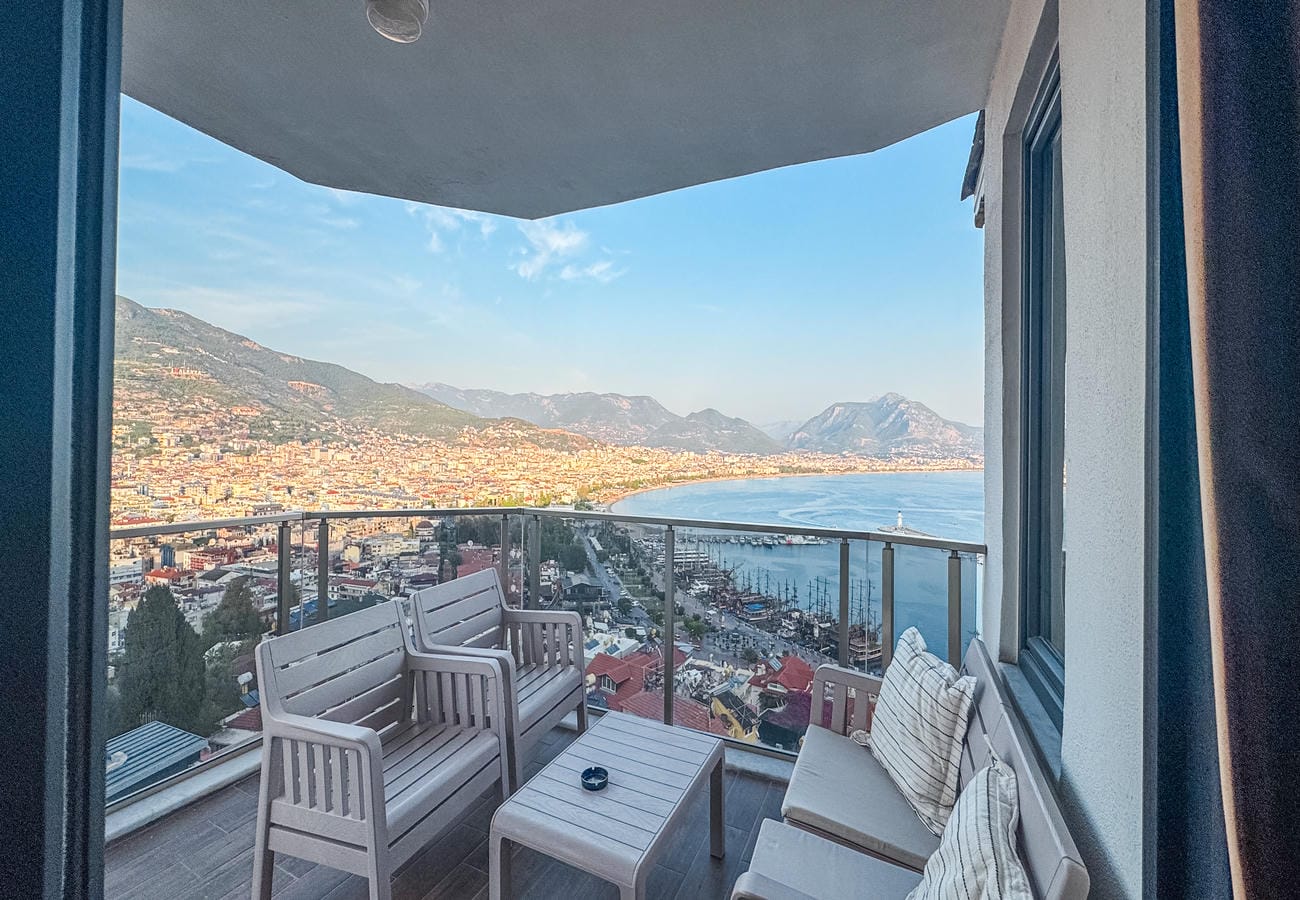 Balcony with glass railing, outdoor sofa and chairs overlooks a bay from an apartment in Alanya