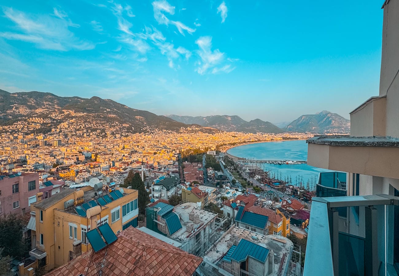 Panoramic sea bay with port piers and red roofs shows an apartment for sale in Alanya