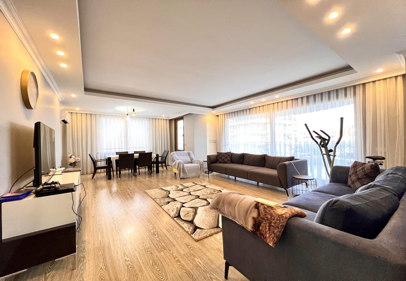 Gri köşe koltuklu salon Çikcilli’deki 4+1 dairede panoramik pencerelerden şehir manzarasına bakıyor