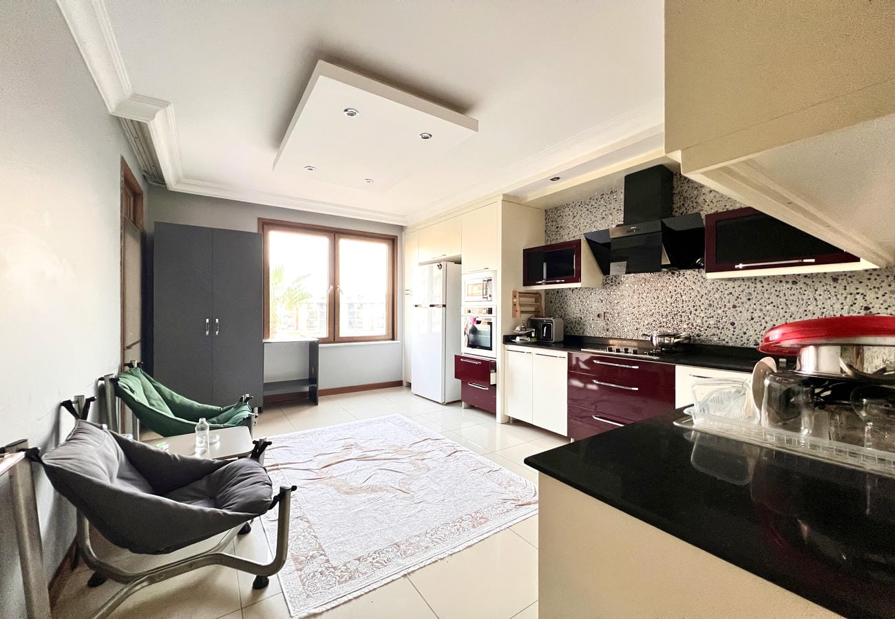 Siyah tezgâhlı, mozaik backsplashli mutfak 4+1 dairenin halılı yemek alanıyla birleşiyor