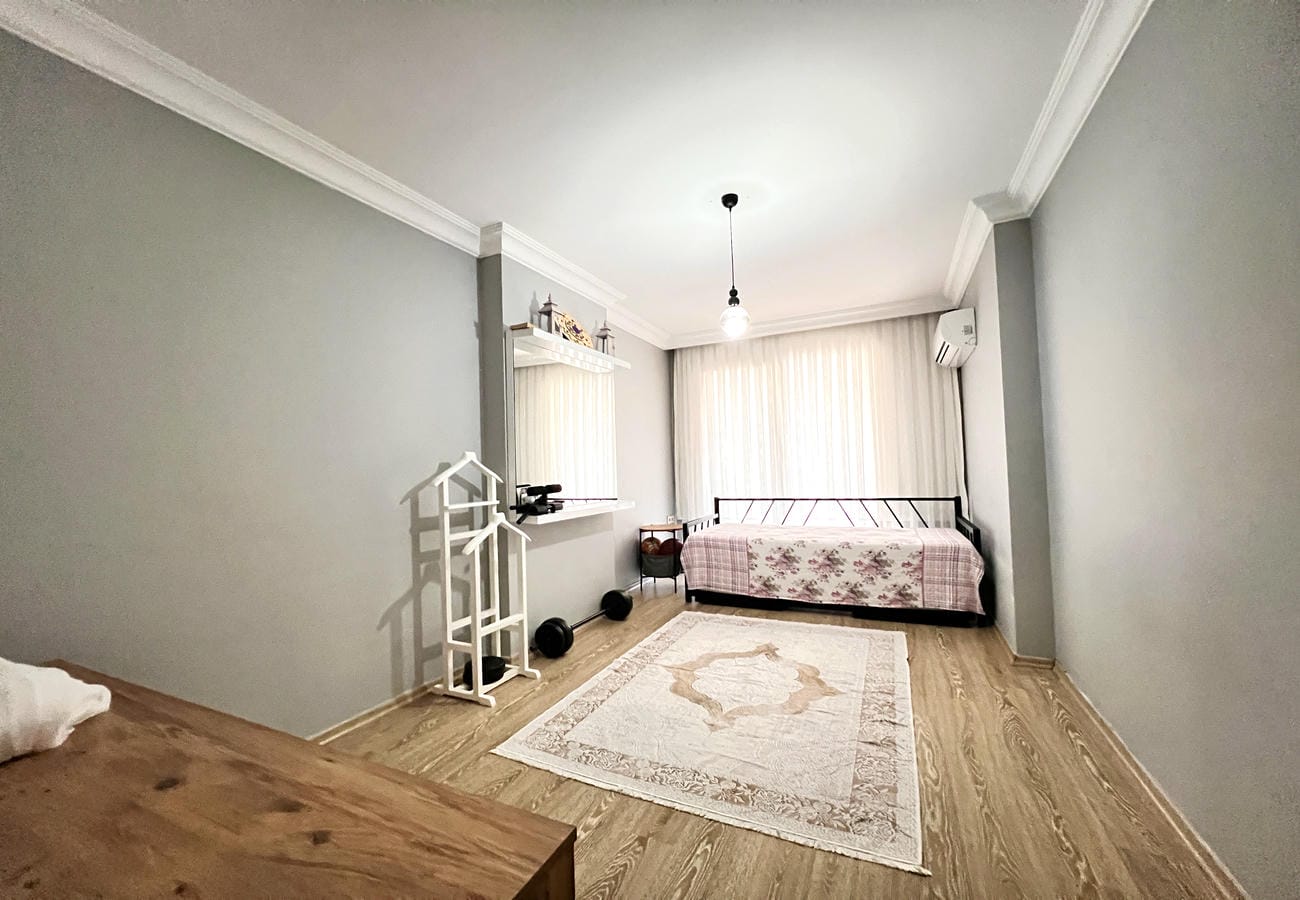 Metal başlıklı ve çiçekli örtülü yatak odası Çikcilli’deki 4+1 dairede geniş pencereyle aydınlanıyor