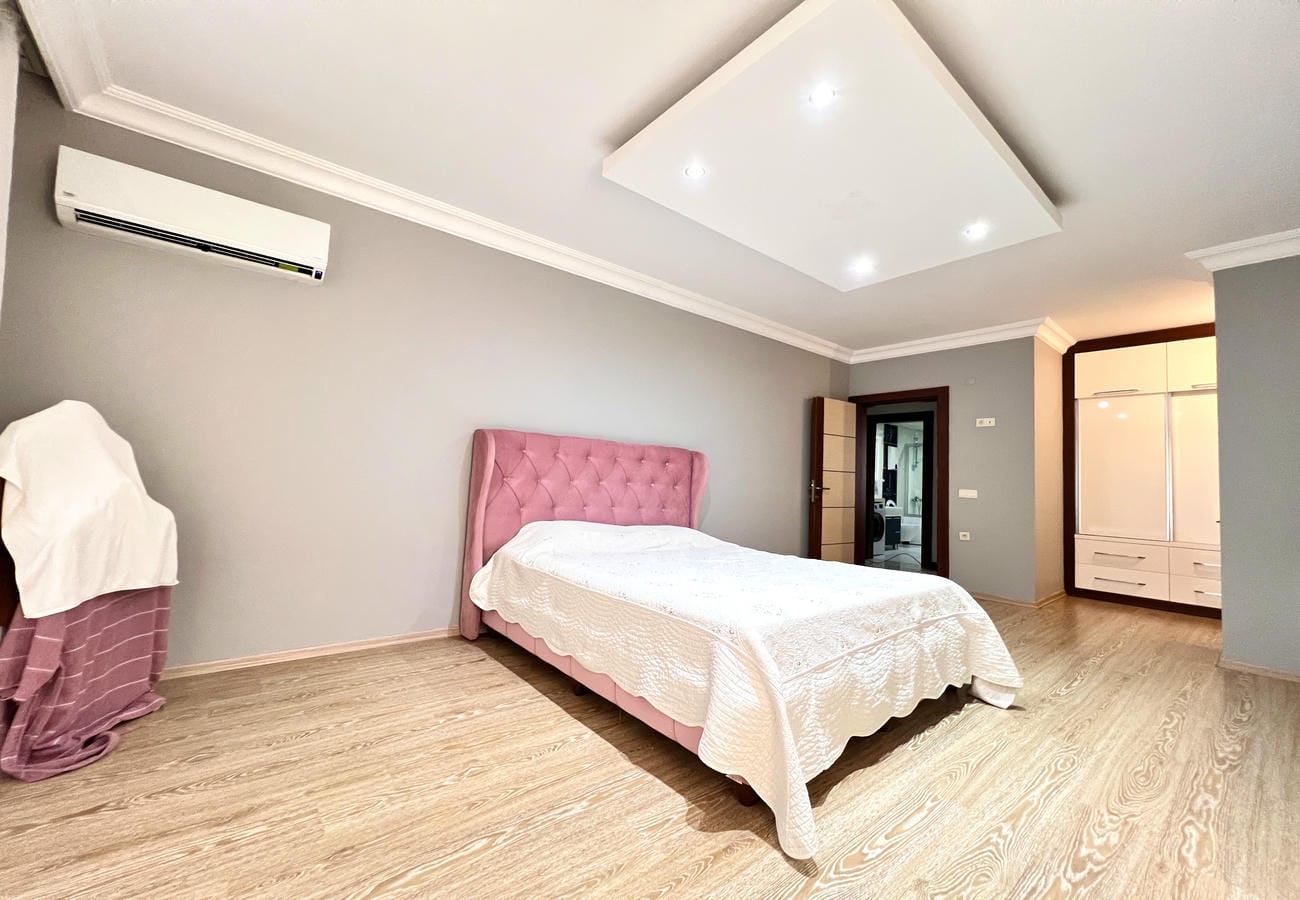 Pembe kapitone başlıklı yatak odası 4+1 dairede beyaz dolap ve koltukla birlikte yer alıyor