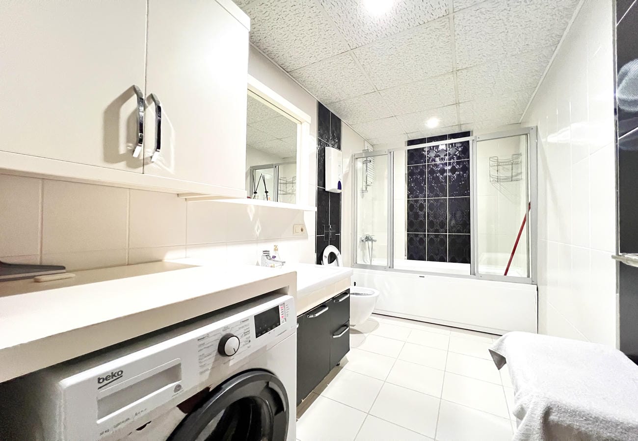 Beyaz küvetli banyo Çikcilli’deki 4+1 konutta cam duş bölmesi ve çamaşır makinesiyle görülüyor