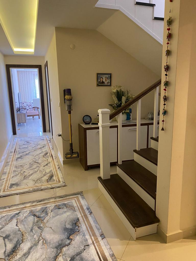Alanya’daki penthouse holünde koyu basamaklı iç merdiven ve konsol üzerindeki çiçekler