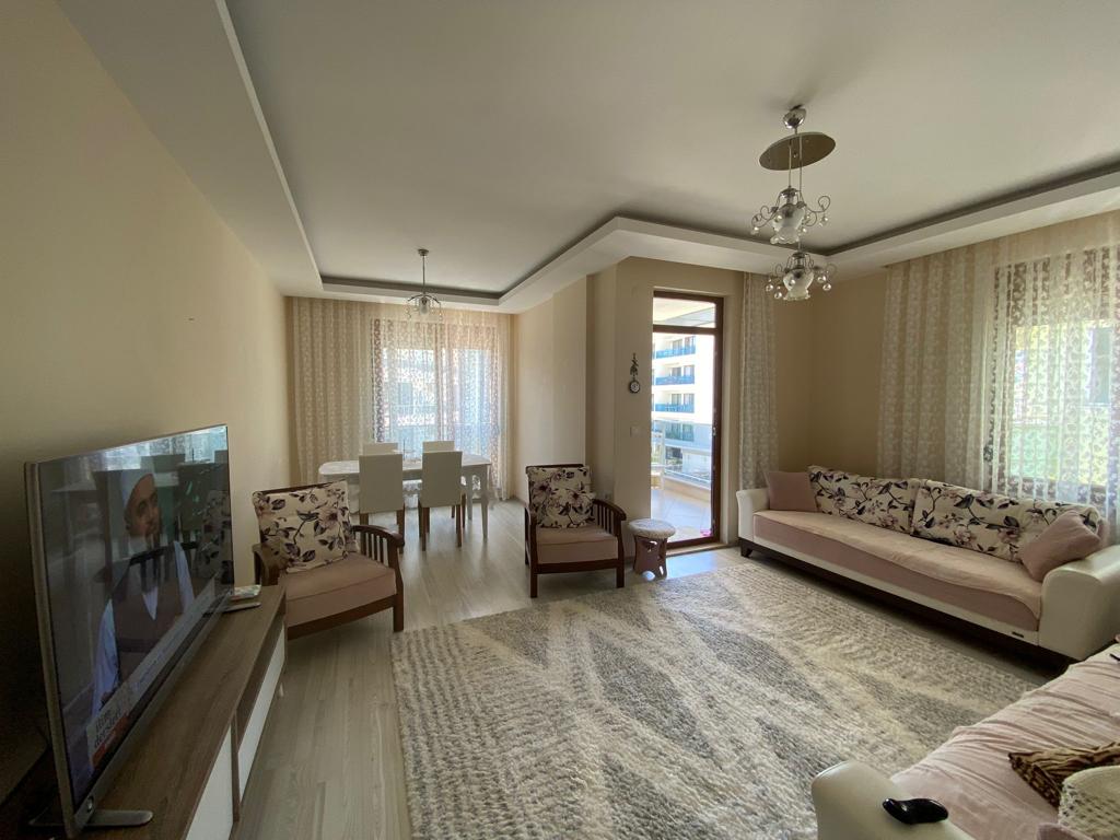 Balkon kapılı mutfaklı salonda Türkiye’de satılık rezidansın koltukları ve yemek masası