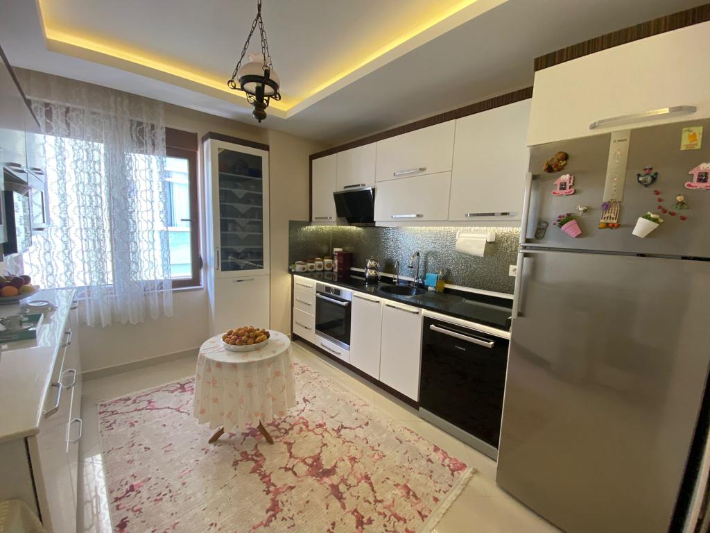 Meyveli yuvarlak masalı beyaz mutfak Alanya’da mozaik backsplash ve gümüş buzdolabıyla