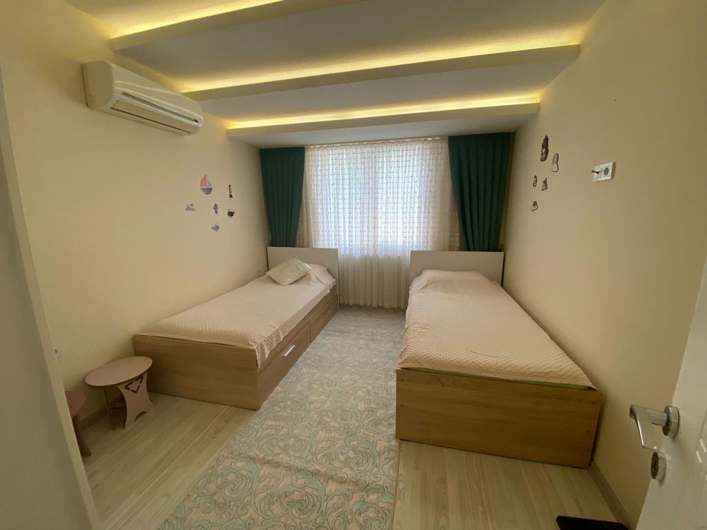 İki tek kişilik yataklı yatak odasında Alanya’daki pencerenin yeşil perdeleri ve duvar kliması