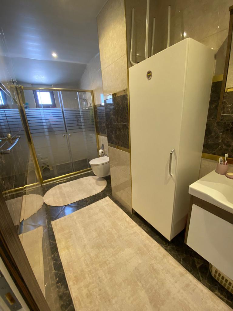 Cam duş kabinli banyoda penthouse için koyu mermer şerit, beyaz lavabo dolabı ve askılı klozet