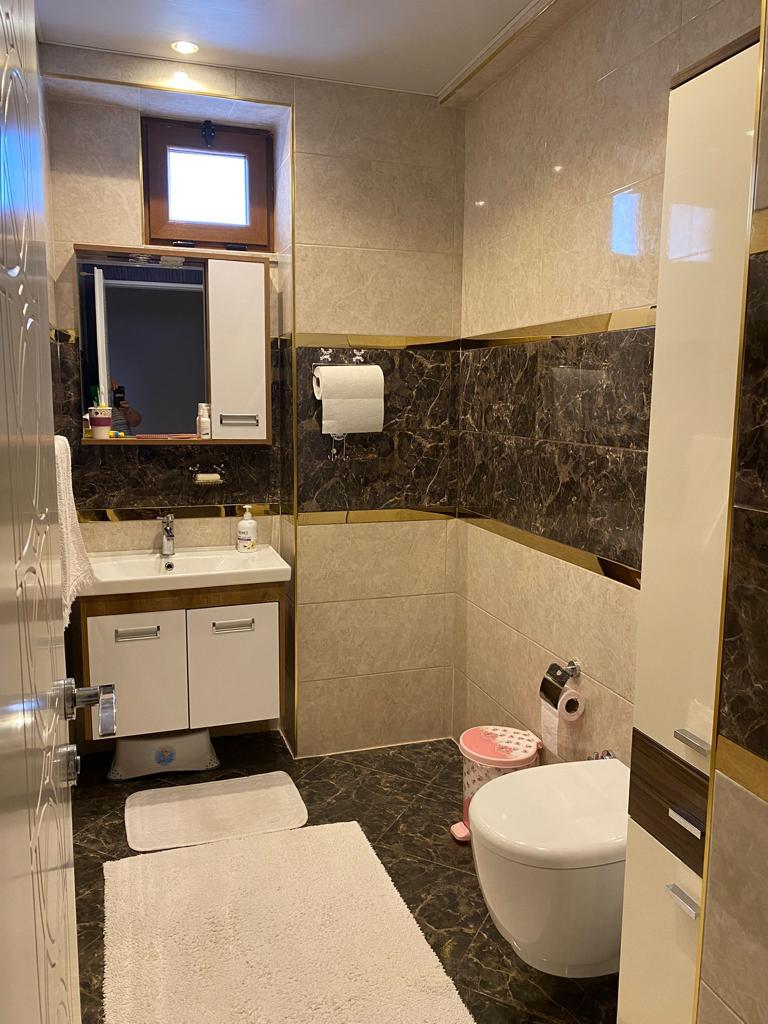 Alanya’daki banyoda aynalı dolap, askılı klozet ve bej duvar fayansları