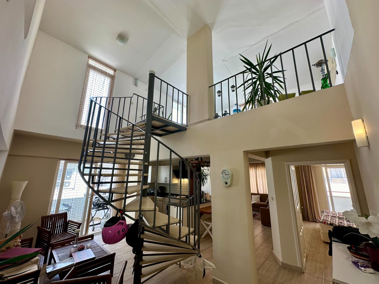 A spiral metal staircase with black railings rises through a double-height space in a duplex in Alanya