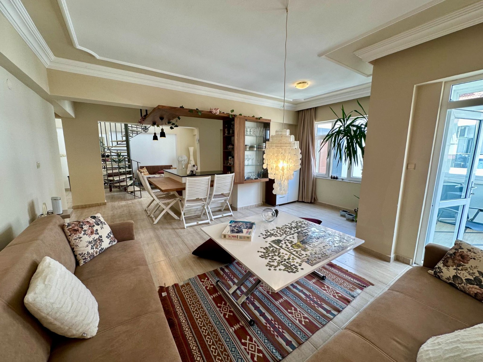A beige corner sofa, dining area and crystal pendant light furnish the living room of a residence for sale in Turkey
