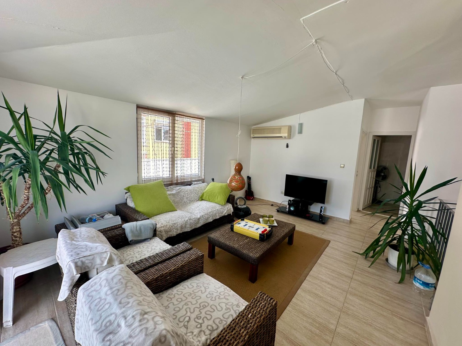 A living room with green cushions, woven armchairs and a window with blinds in a residence in Alanya