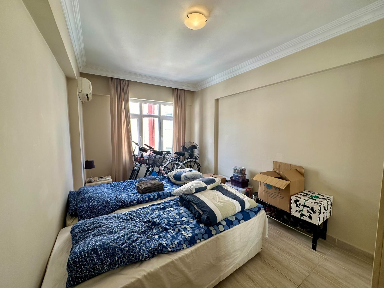 Two single beds, bicycles and a bench stand beside the window in a bedroom near the sea