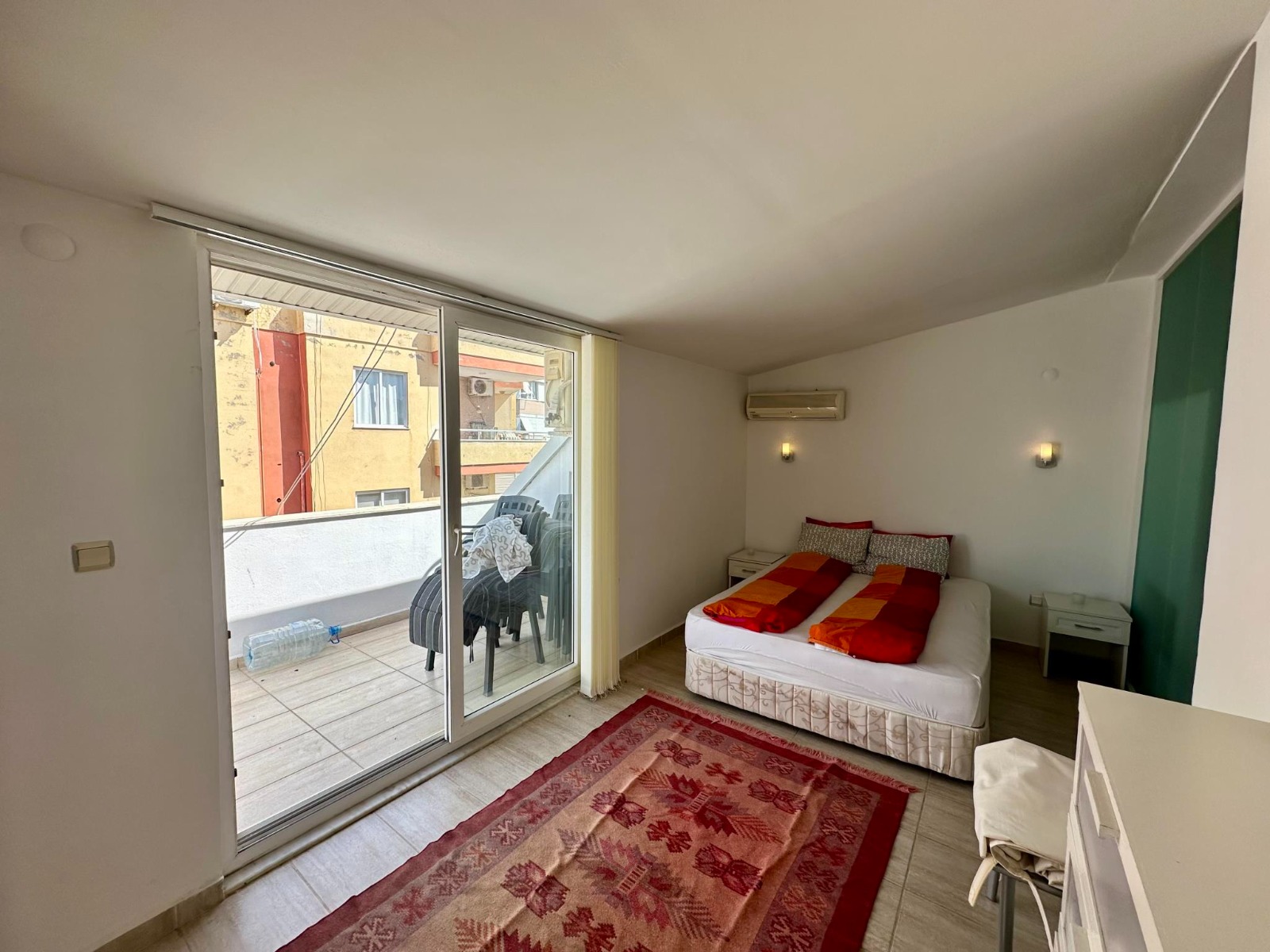 A double bed and balcony with outdoor chairs furnish the bedroom of a duplex