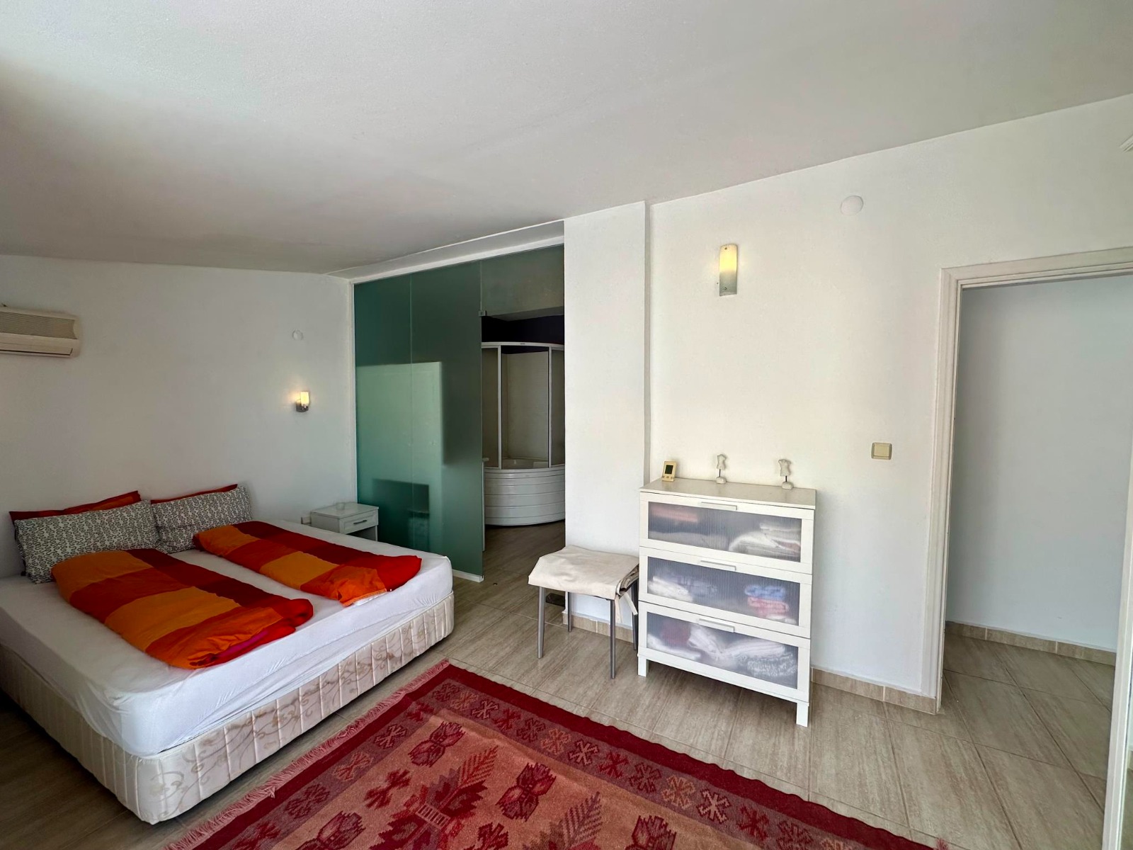 A double bed, red patterned rug and dressing-room door furnish the bedroom of a residence in Alanya
