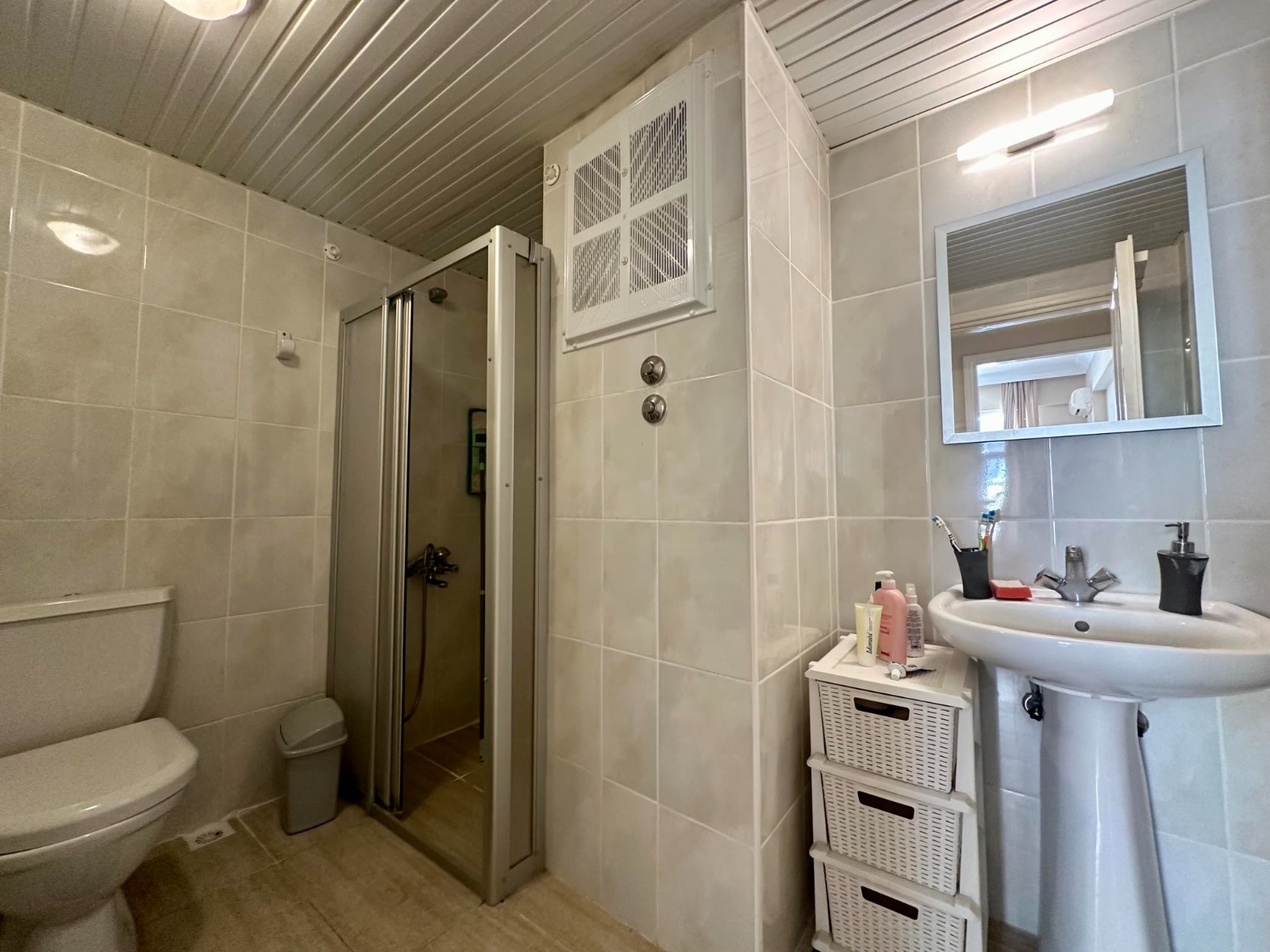 Beige wall tiles and a glass shower enclosure feature in the bathroom of a penthouse