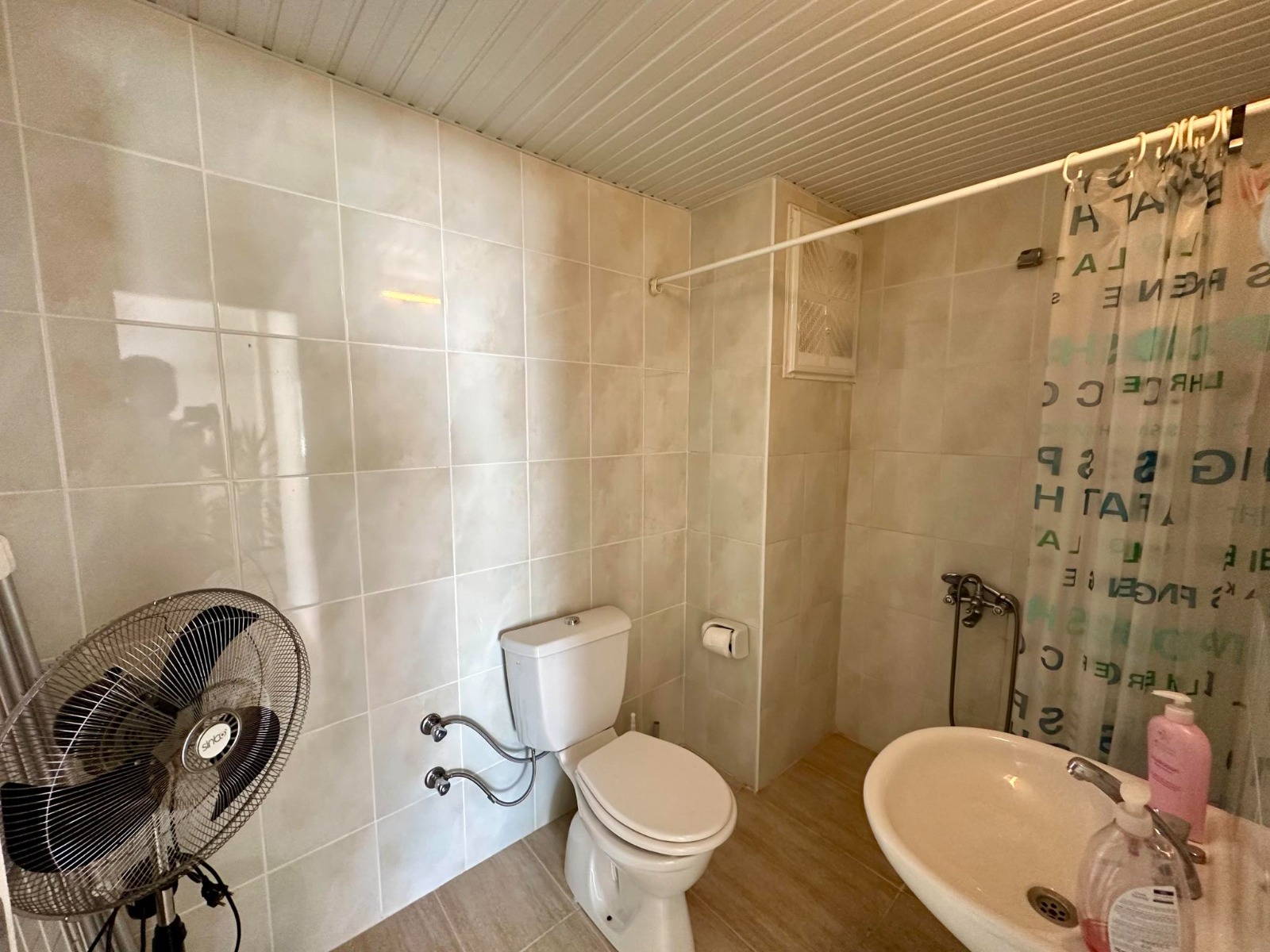A curtained shower area, sink and floor fan feature in the bathroom near the sea