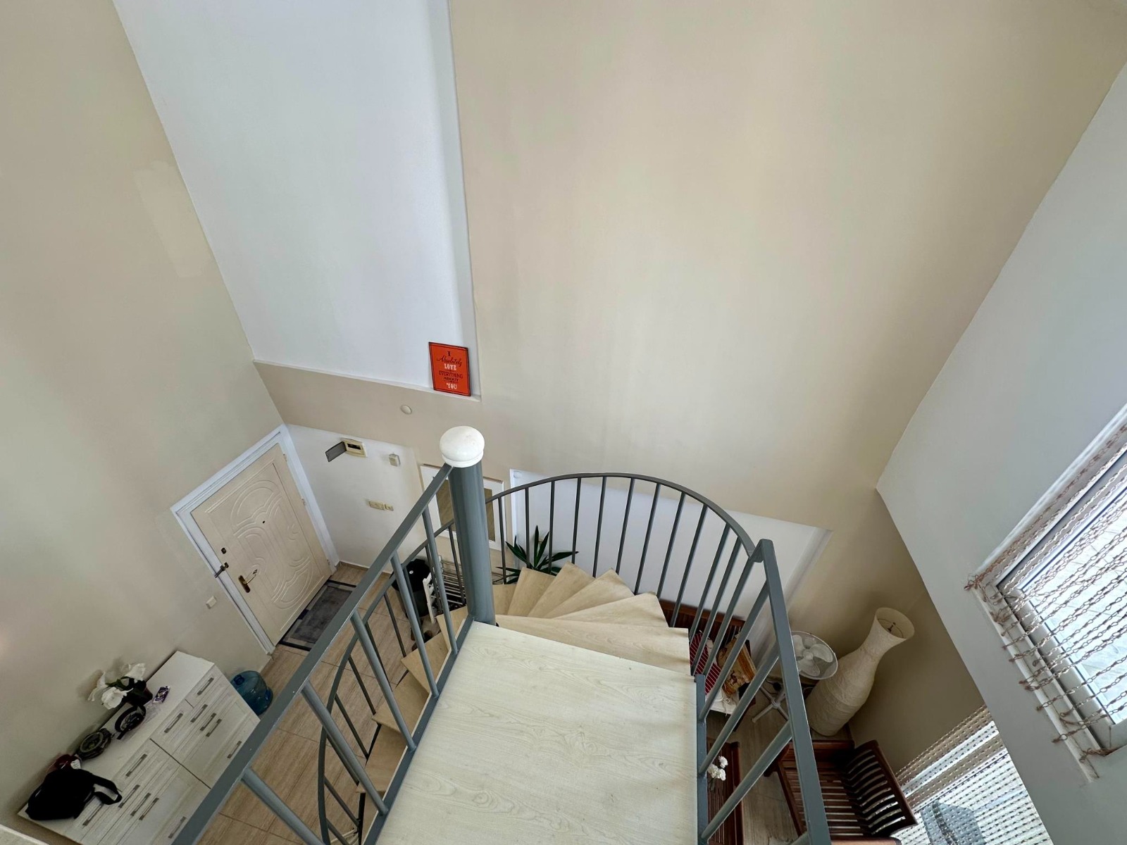 A spiral staircase with wooden steps and metal railings rises through a duplex