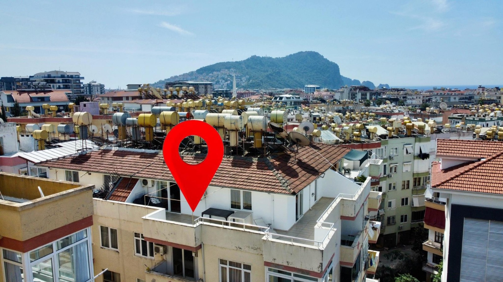 Dense city buildings with mountains and sea beyond frame a 4+1 top-floor apartment for sale in Turkey