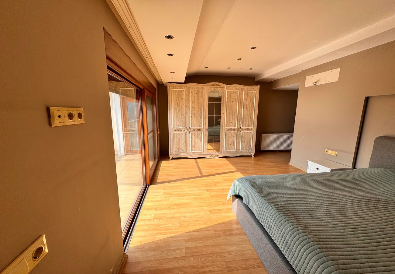Dairenin yatak odasında aynalı bölümlü açık renk dolap ve sürgülü balkon kapısı
