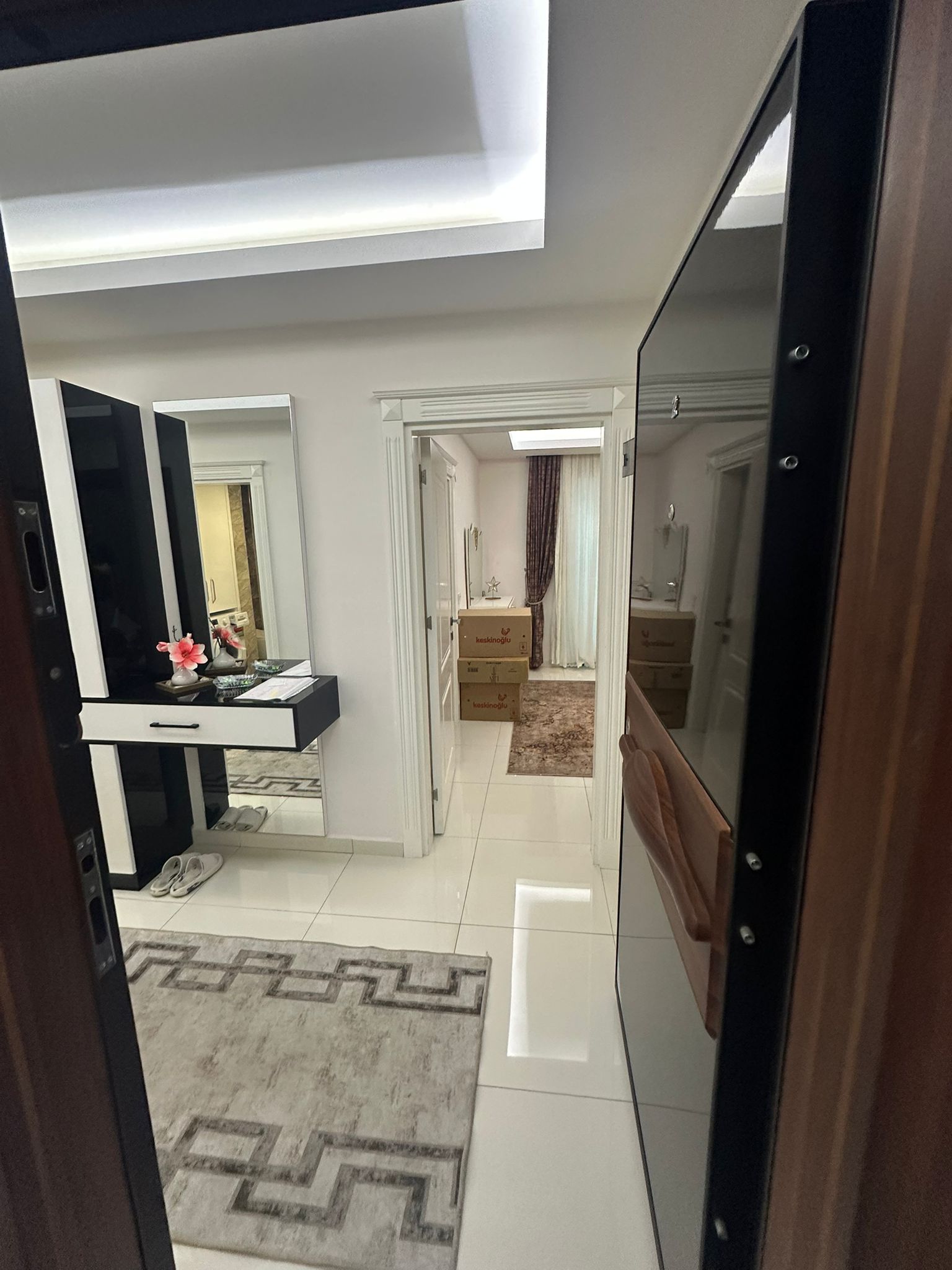 Alanya’daki dairenin antre bölümünde koyu ahşap kapı, gri desenli halı ve aynalı konsol