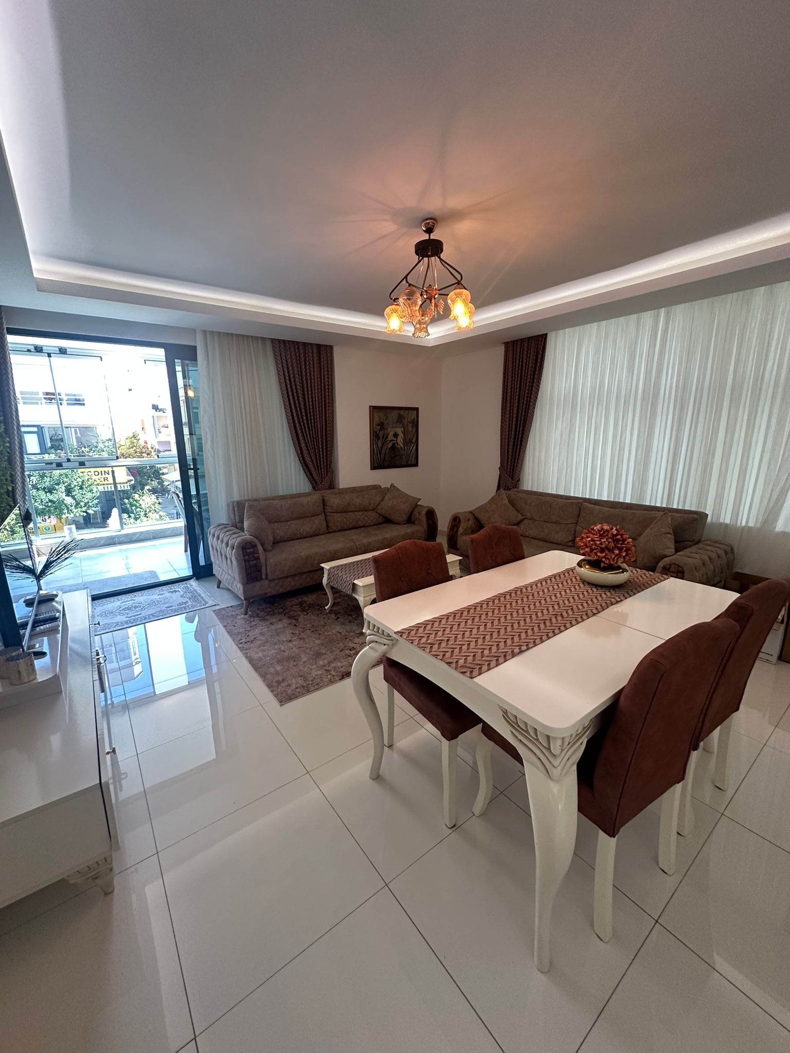 Türkiye’deki dairenin mutfaklı salonunda beyaz yemek masası, bej koltuklar ve balkon kapısı