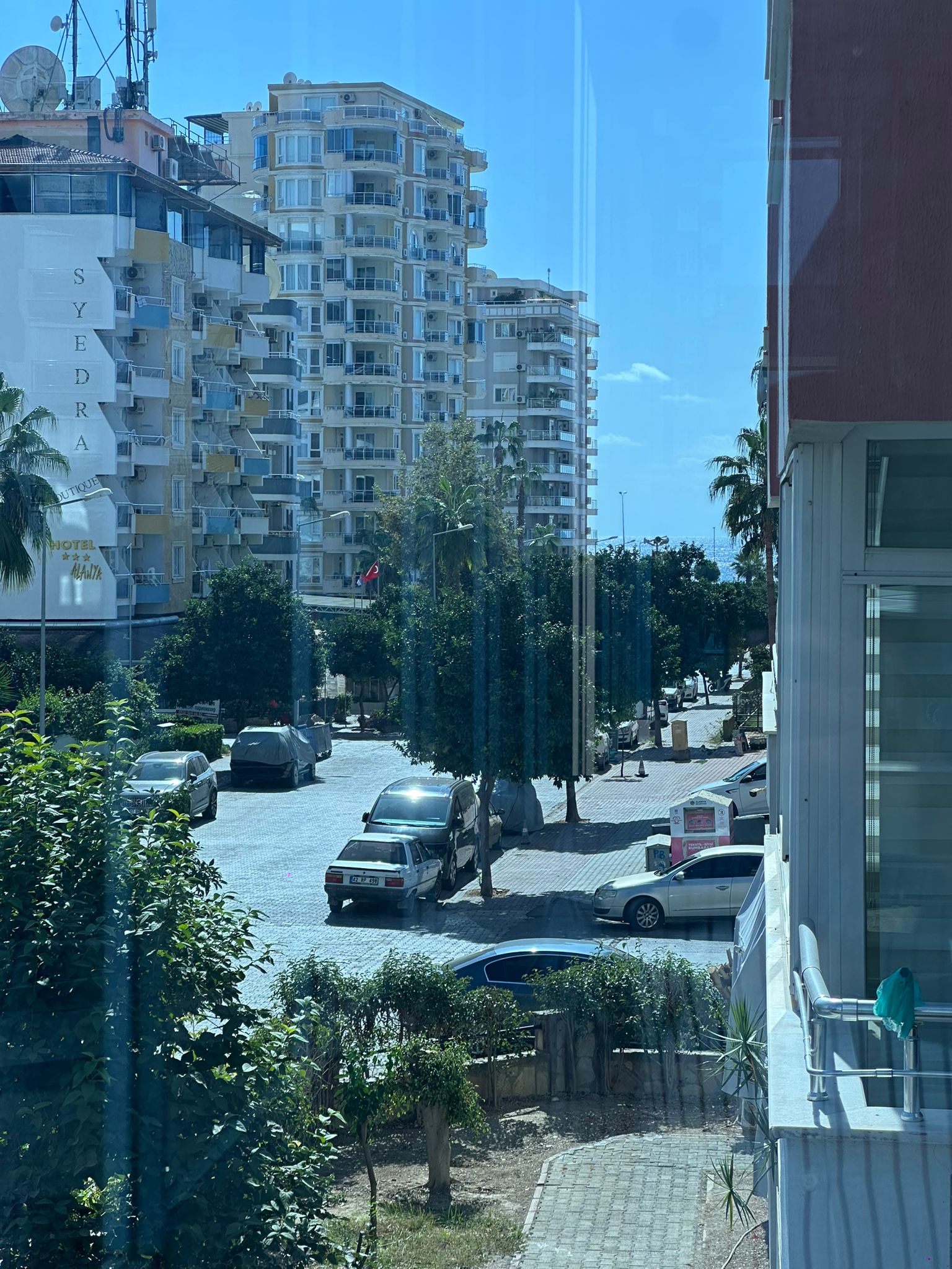 Alanya’da palmiye ağaçlı şehir sokağı, yüksek binalar ve uzakta denize açılan boşluk