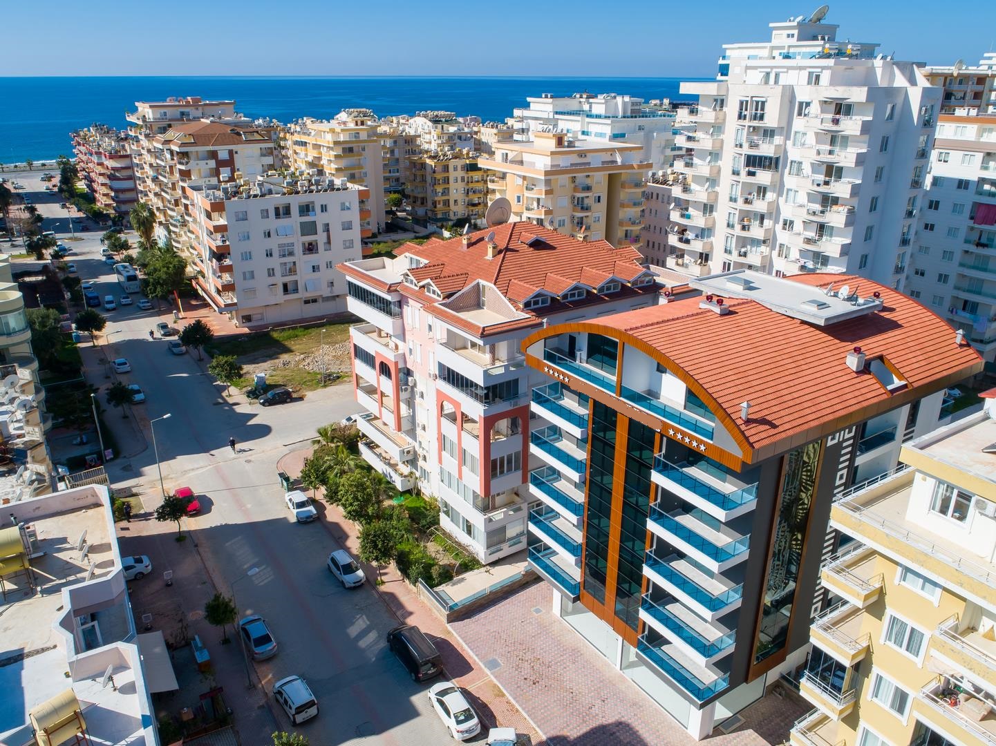 Kıvrımlı kırmızı çatılı binanın havadan görünümü, Türkiye’de satılık dairelerin bulunduğu yerde deniz ufukta
