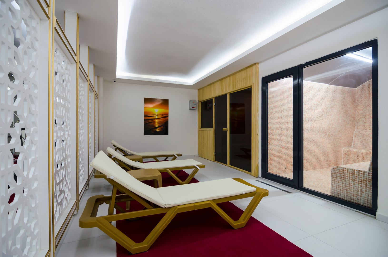 Mahmutlar’da spa alanında beyaz minderli ahşap şezlonglar ve buhar odasına cam kapı