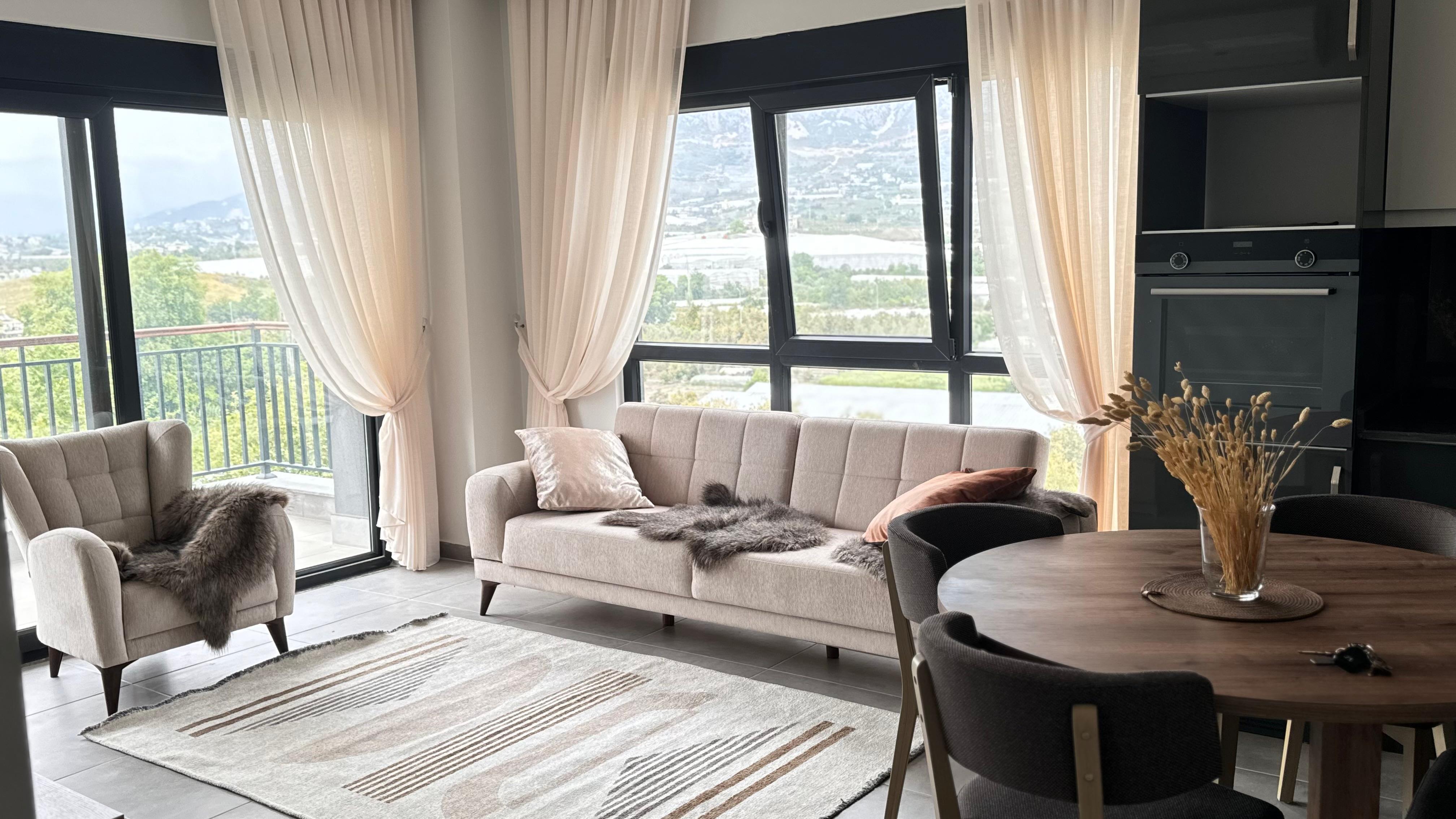 Mutfak-salon görünümünde denize yakındaki 1+1 dairede açık renk kanepe, koyu mutfak ve balkon kapısı