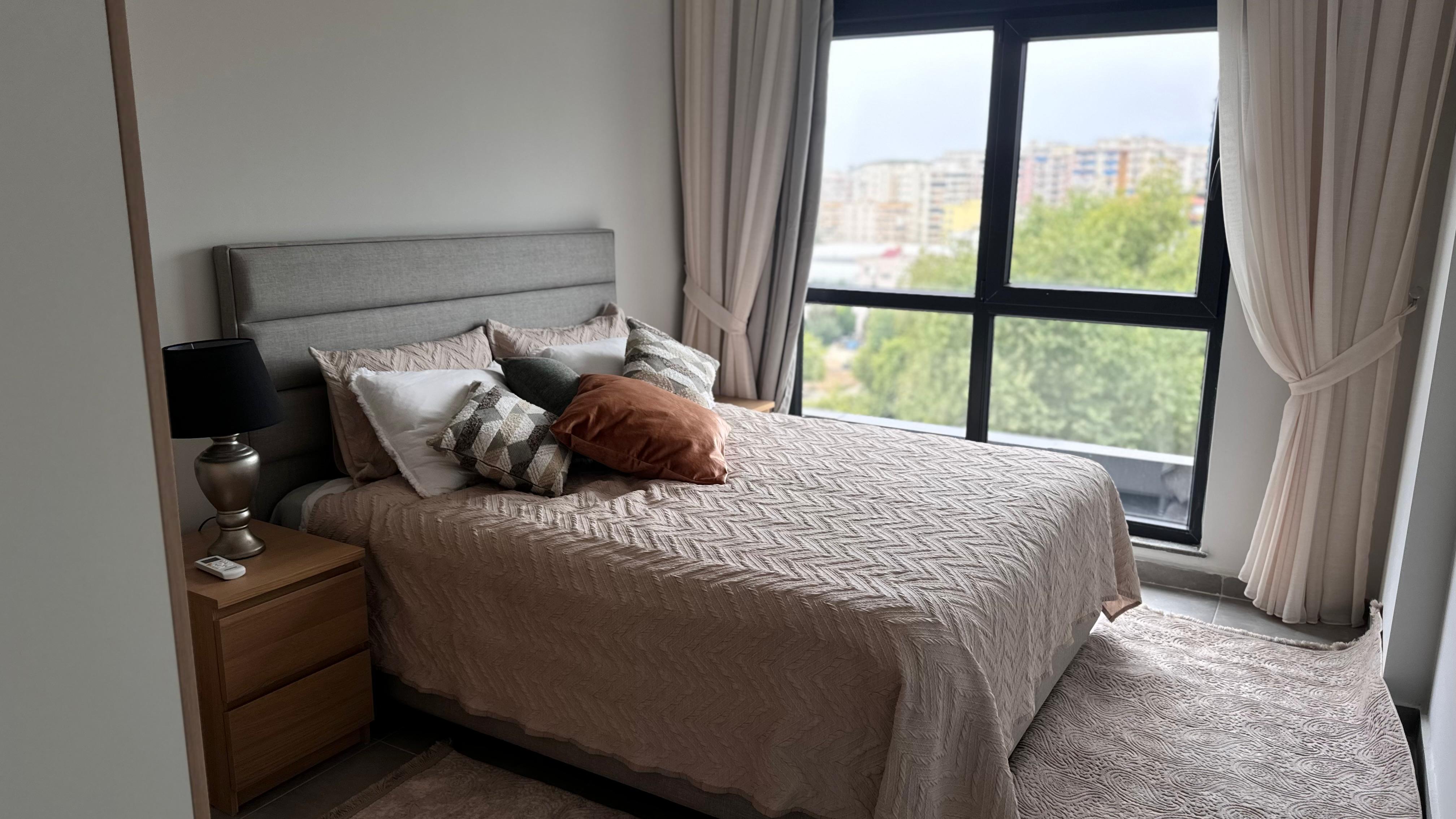 Yatak odasında gri başlıklı çift kişilik yatak ve panoramik pencere, rezidans dairesinin içinde