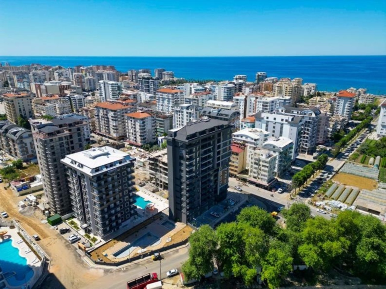Denize yakın rezidansta iki yüksek blok, açık havuz ve ufuktaki mavi deniz, Türkiye'de
