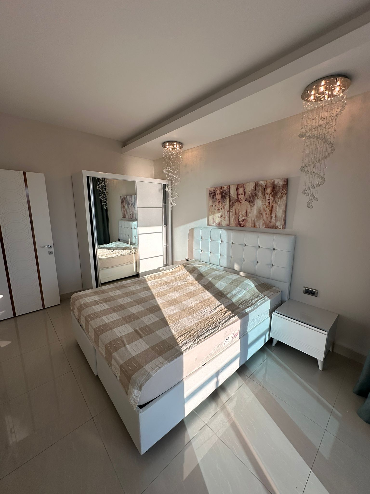Apartman dairesinin yatak odasında çift kişilik yatak, kareli örtü ve aynalı kapaklı dolap