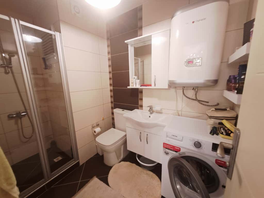 Duş kabinli banyo, çamaşır makinesi ve bej kahverengi duvar karolarıyla Alanya’daki dairede