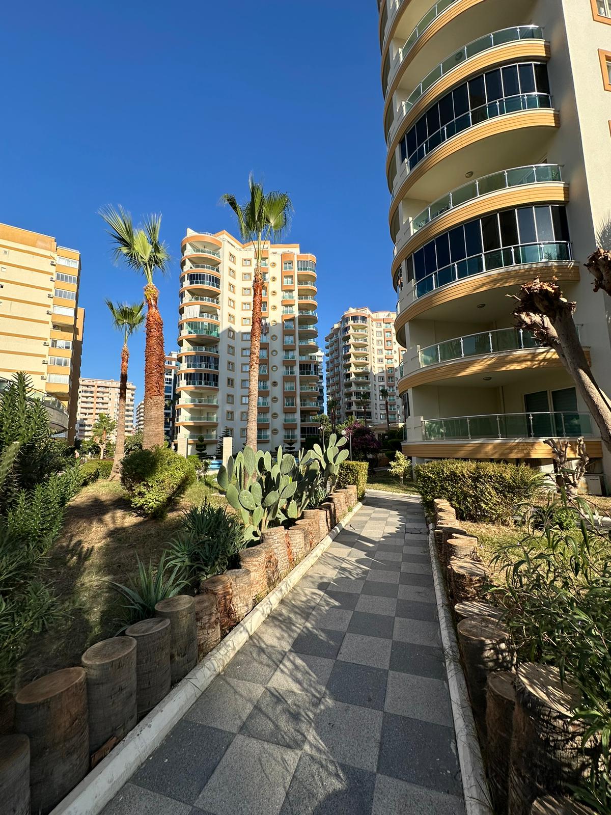 Palmiyeli gri taş yol ve kaktüs çiçekliği, Alanya’da Türkiye’deki konut blokları arasında