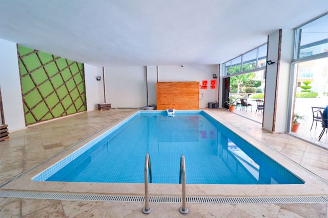 Panoramik pencereli kapalı havuz ve ahşap duvar, Alanya’daki apartman kompleksinde