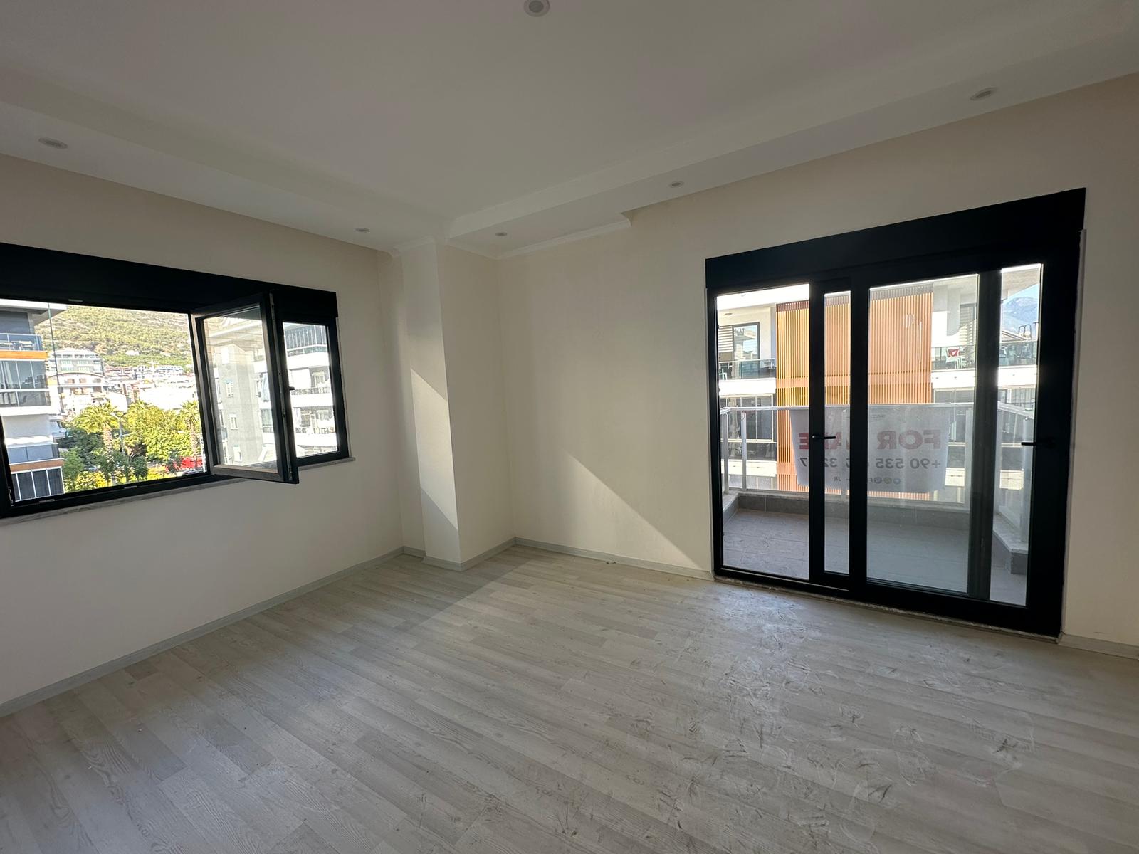 Alanya’da satılık 2+1 dairenin salonunda balkon kapısı ve geniş siyah çerçeveli pencere