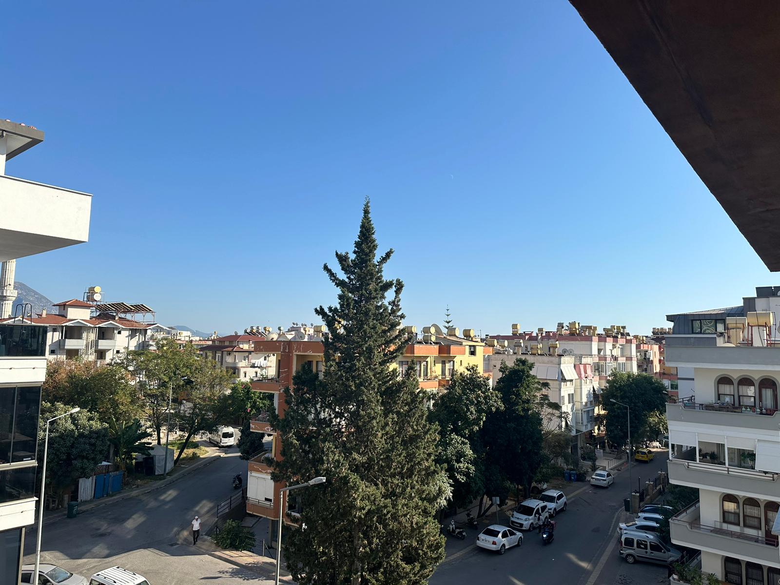 Türkiye’de satılık dairelerin bulunduğu çevrede çam ağacı, balkonlu apartmanlar ve şehir sokağı