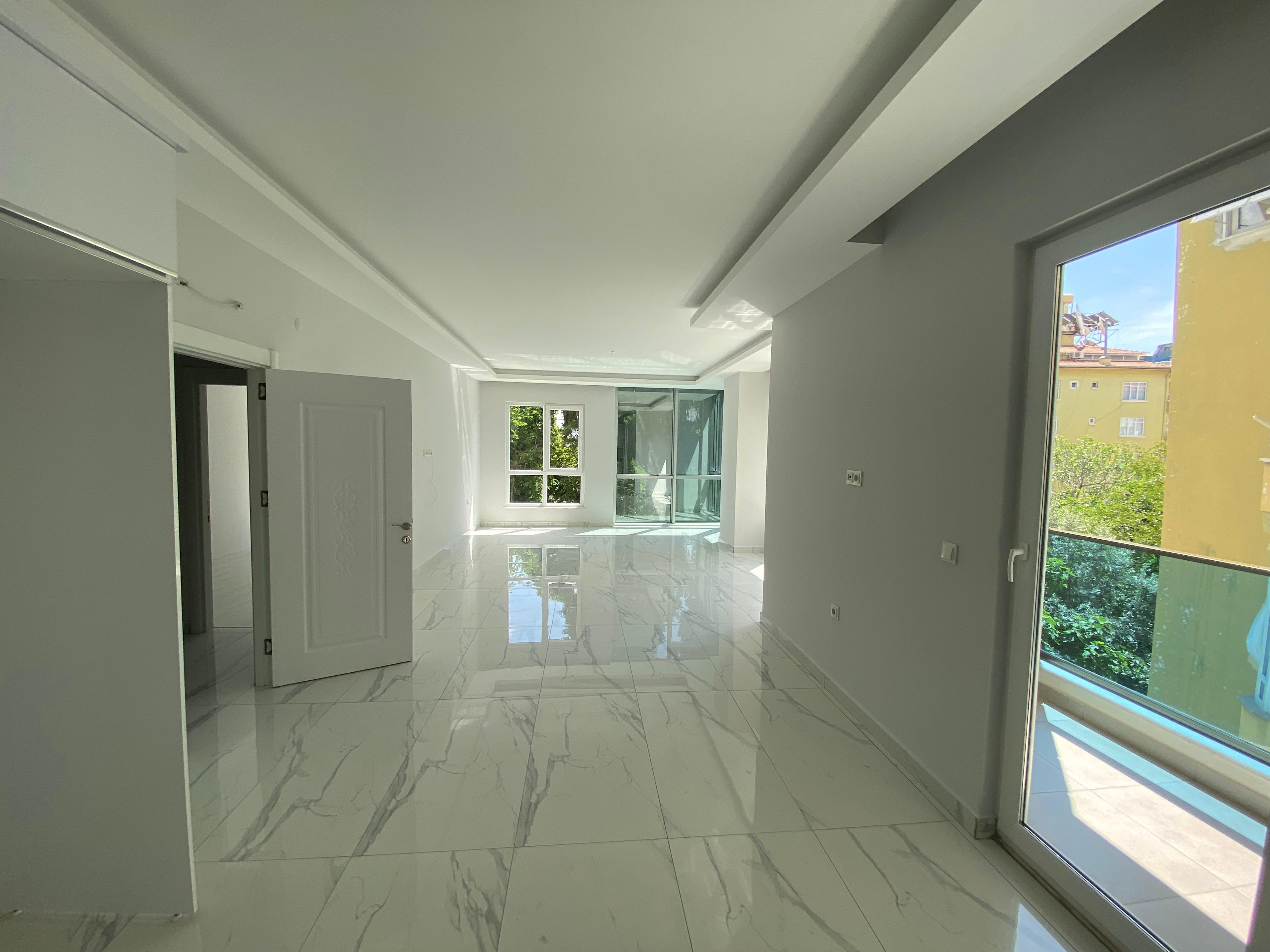Alanya’da mutfaklı salonda panoramik balkon kapısı, geniş pencere ve sarı cephe manzarası