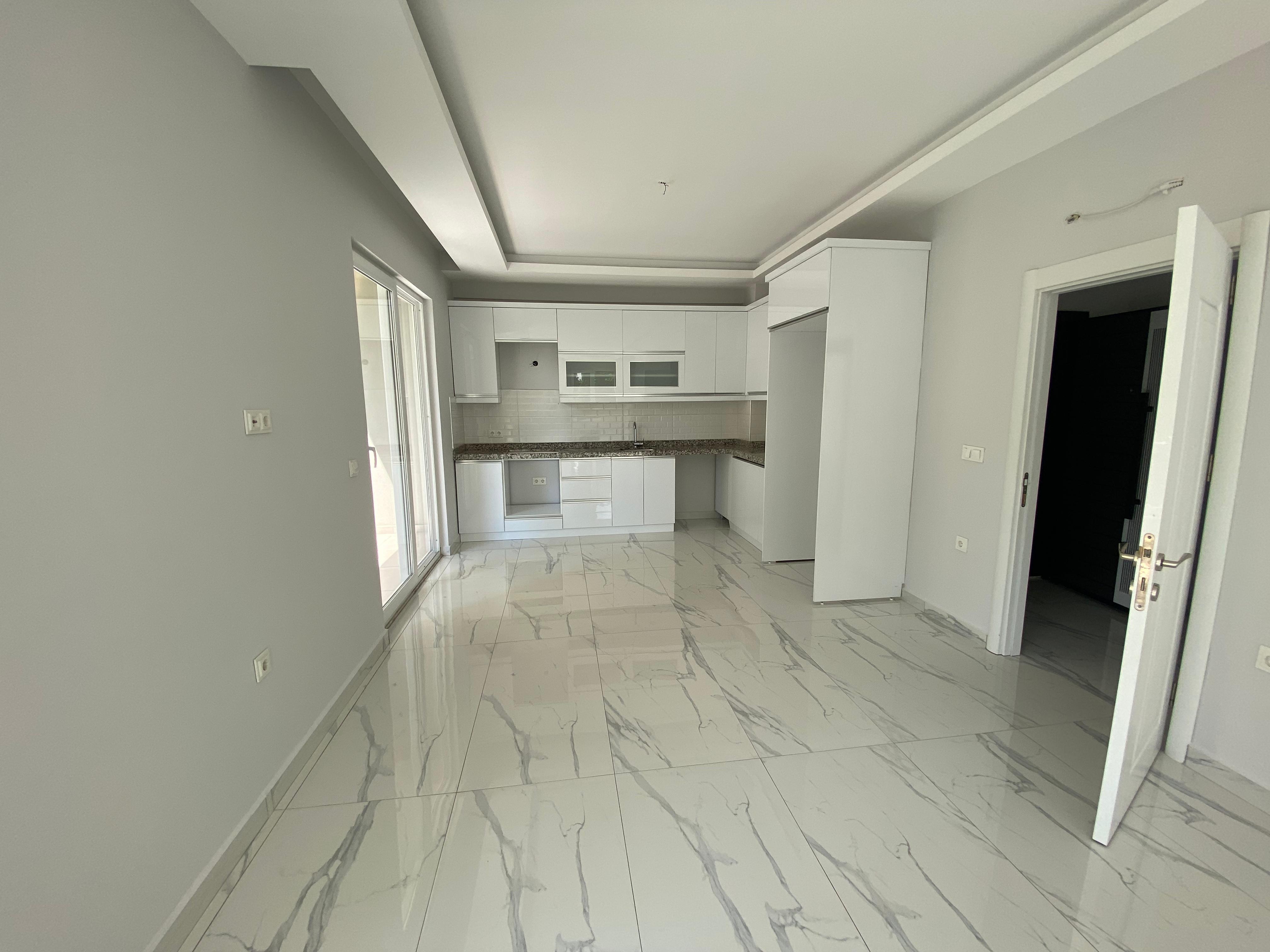 Alanya’daki konutun mutfağında beyaz köşe dolaplar, koyu granit tezgâh ve balkon kapısı