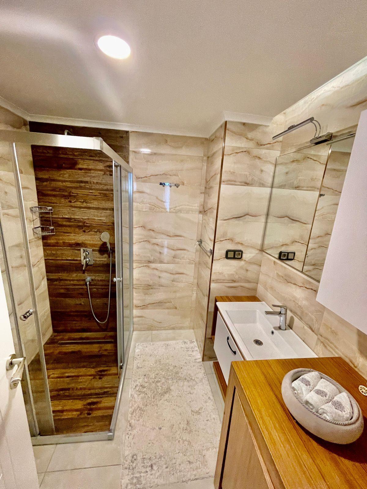Banyoda cam duş kabini ve ahşap tezgâhlı lavabo, Alanya’daki dairenin içinde
