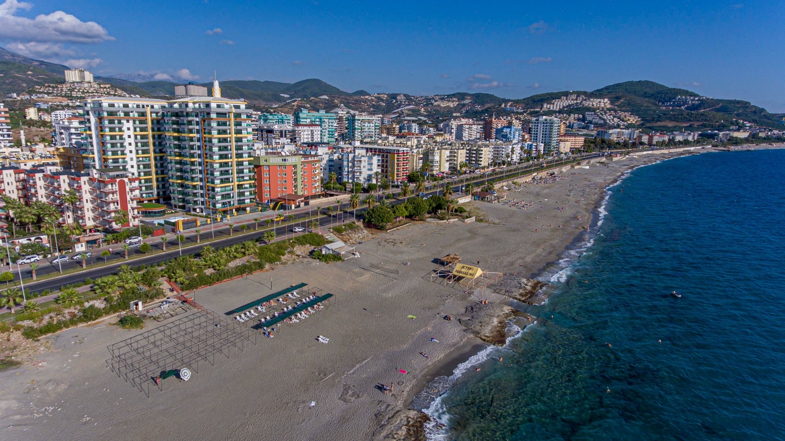 Türkiye’de satılık dairelerin bulunduğu kıyıda çakıllı plaj, mavi deniz dalgaları ve yüksek konutlar